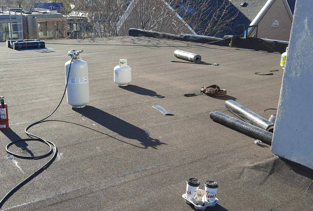 Roofers in Toronto installing torch‑on cap sheet on a flat roof